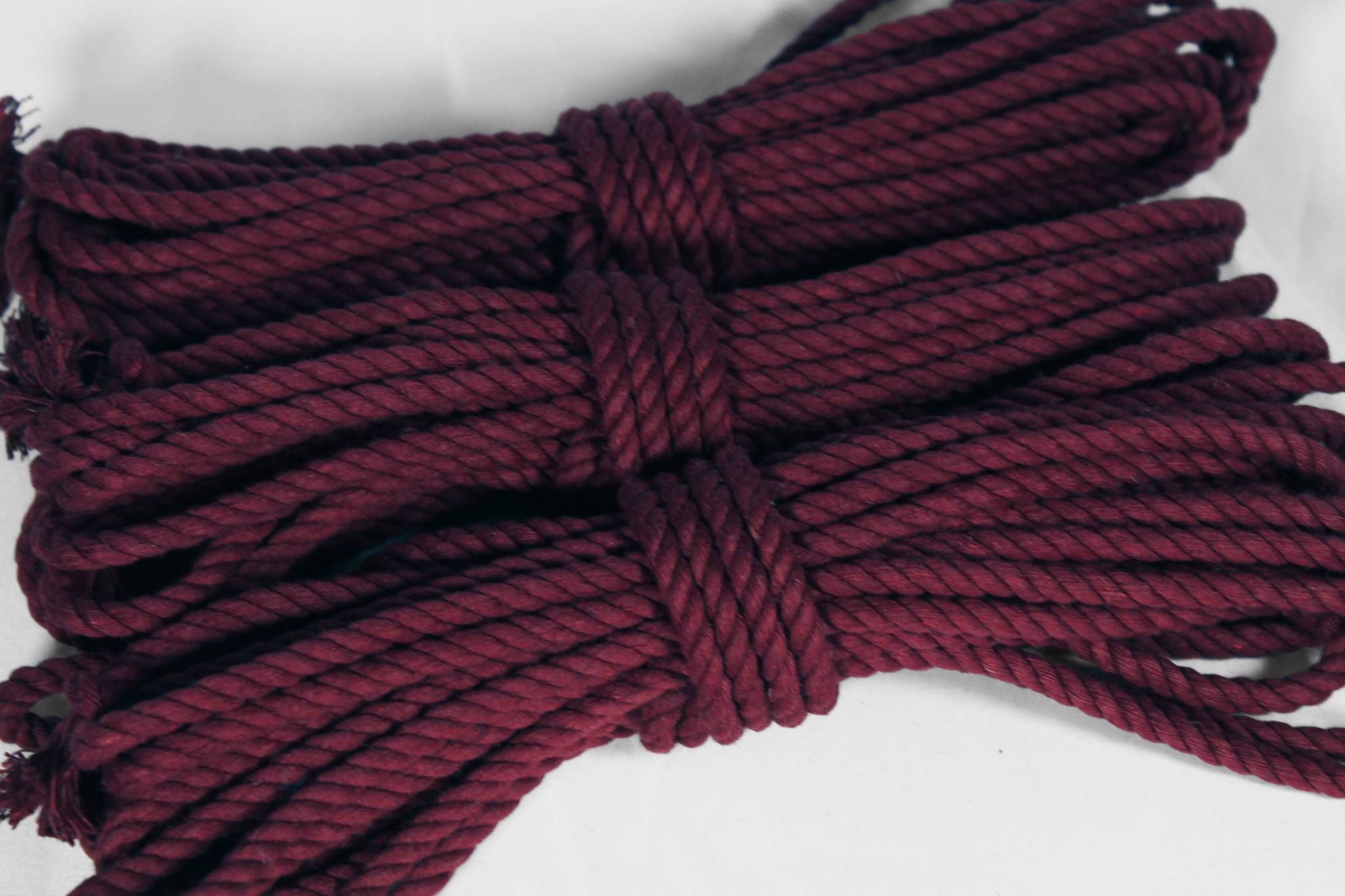 A bundle of thick twisted cotton rope in a deep burgundy or maroon colour, tied in the centre, photographed on a plain white background.