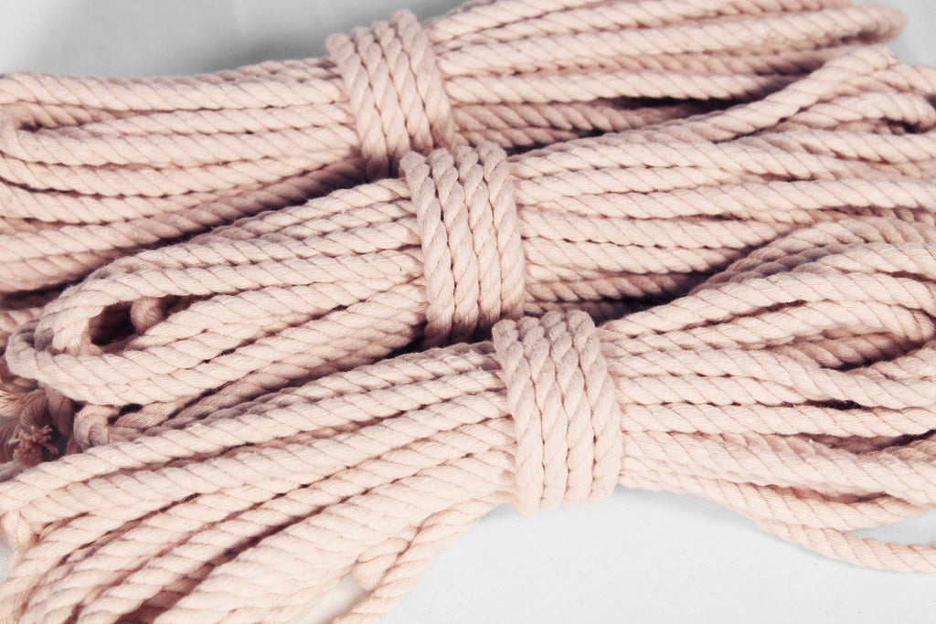 A close-up of several coiled strands of thick twisted rope in a pale blush pink color, arranged on a light neutral background.