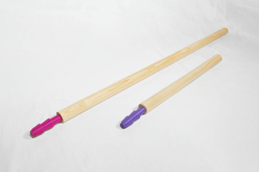 Two long light wood poles with colored plastic ends, one pink and one purple, laid diagonally on a white fabric background.